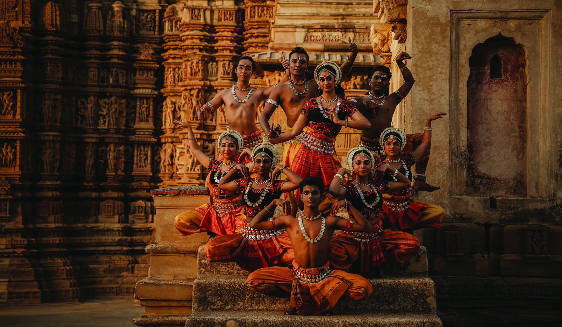 Sutra dancers in orange and red Odissi costumes posed against carved temple architecture