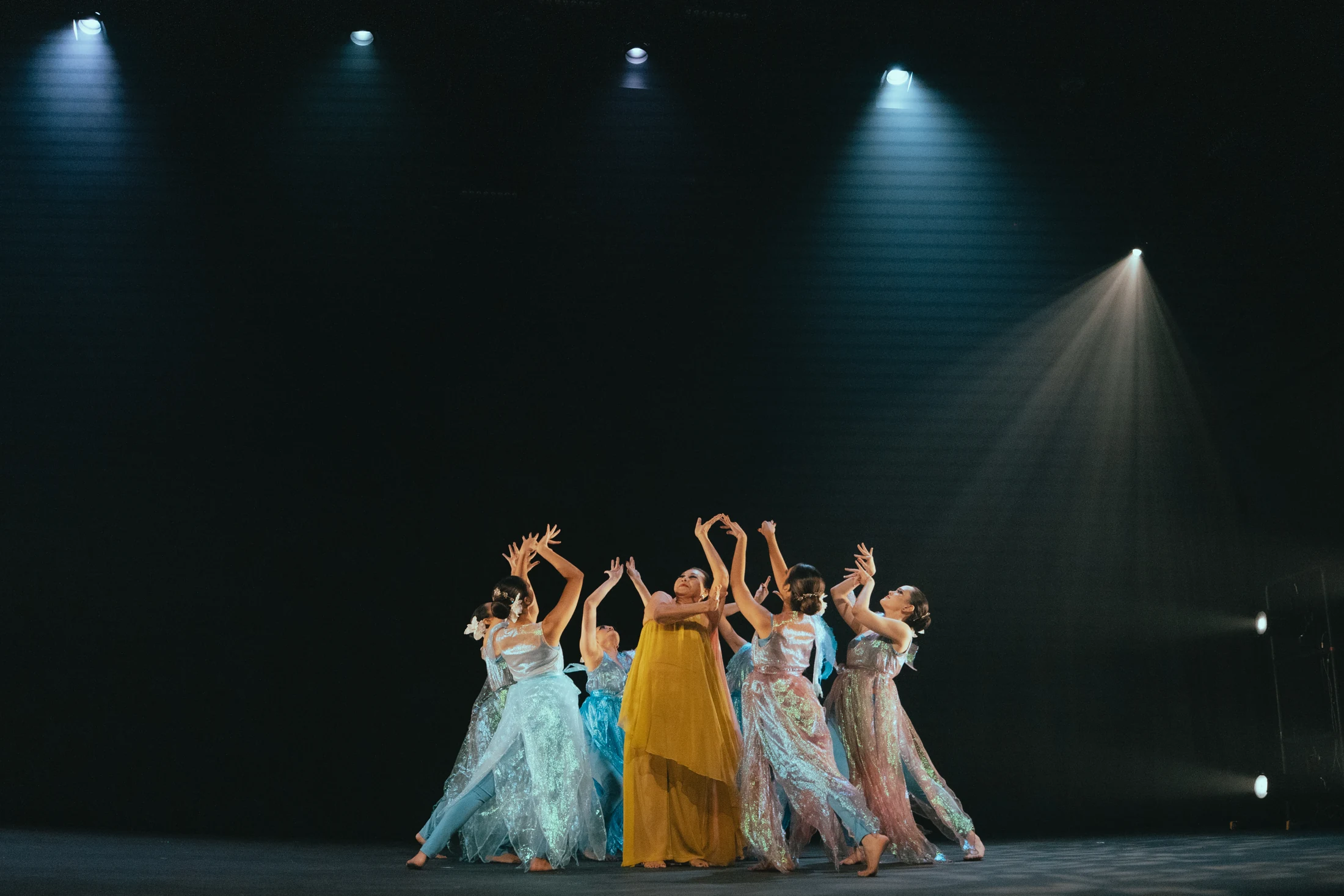Kelopak dancers in blue and silver surround a performer in yellow beneath stage spotlights