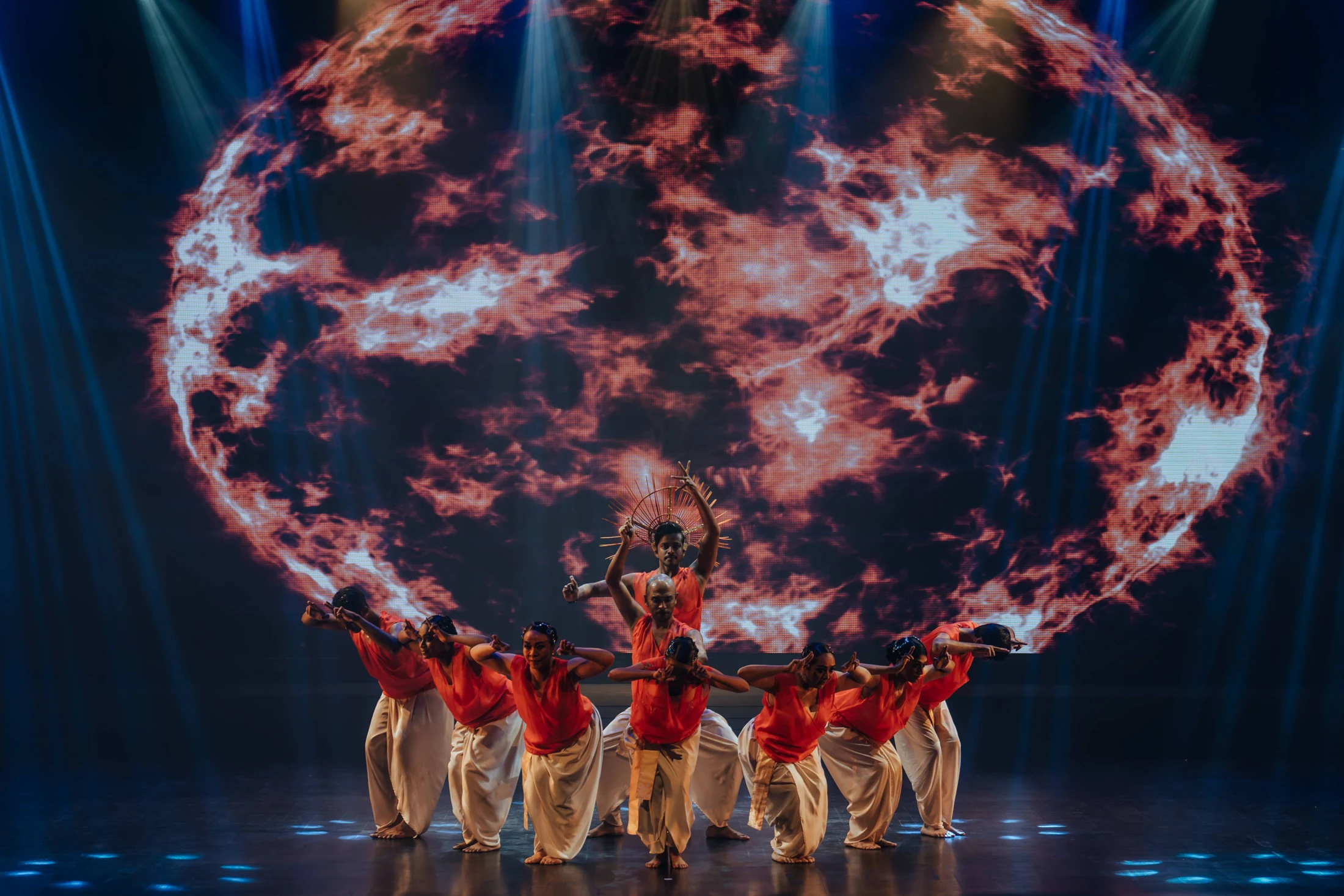 An ensemble dances before a glowing cosmic projection